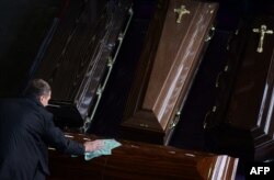 Сотрудник компании, производящей гробы, протирает гробы, представленные на ежегодной выставке "Некрополь" в ВВЦ в Москве, фото AFP